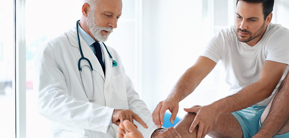 Male-physician-examining-male-patient’s-ankle