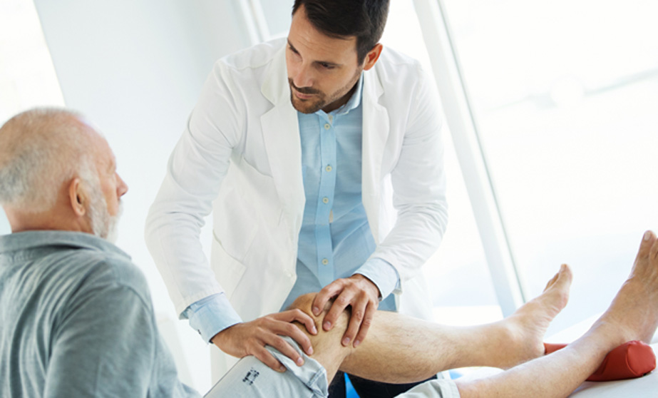 Male-physician-examining-male-patient’s-knee